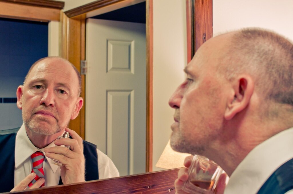 man spraying perfume on neck in bathroom mirror