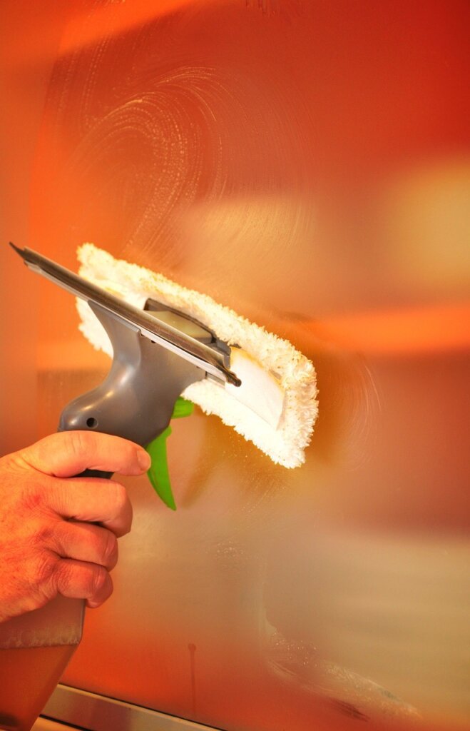 hands cleaning window glass with microfiber cloth before applying insulation sheet